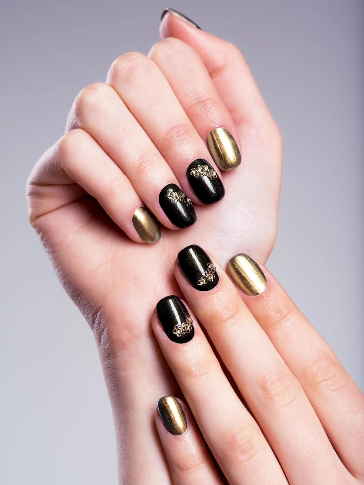 Short nails in glossy black and metallic gold with delicate golden ornaments