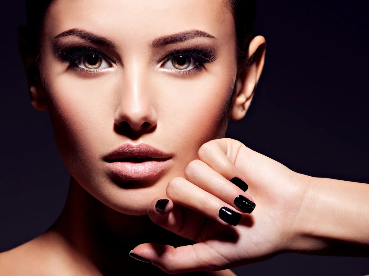 Portrait of a woman with dramatic make-up and glossy black nails against a dark background