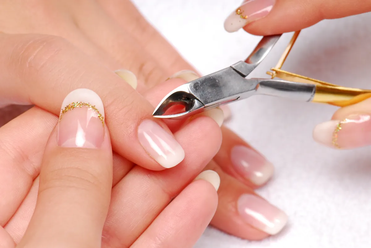 Cuticle care with a small steel nipper at the base of a nail