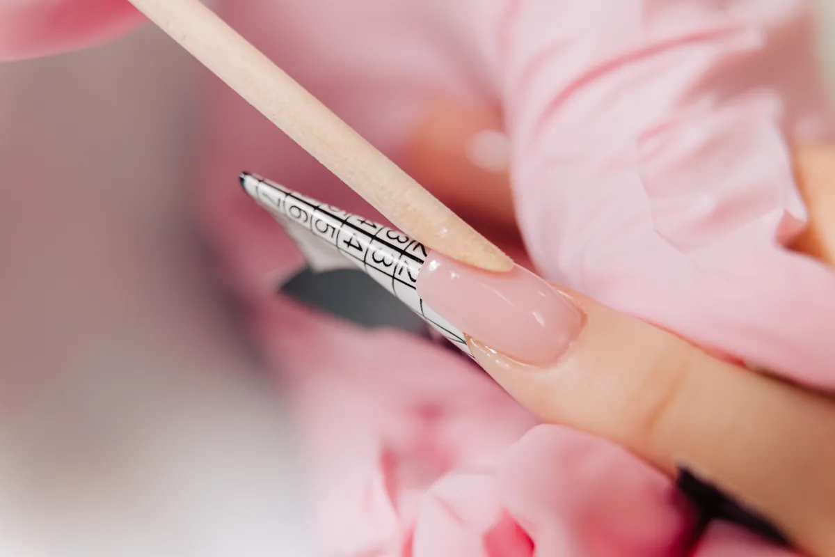 A nail technician shaping a gel extension with a wooden stick
