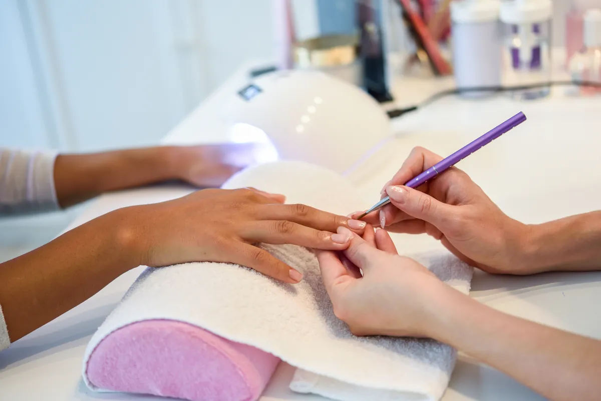 A technician painting gel polish next to an LED nail lamp in a salon