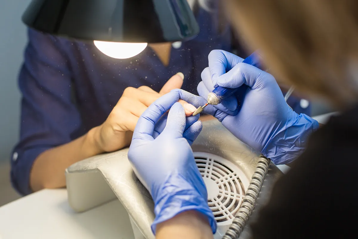 A technician removing old gel polish with an electric nail file