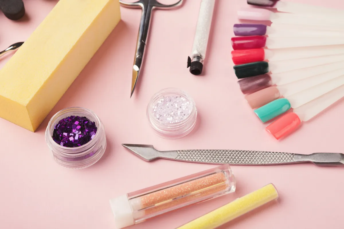 Manicure tools, glitter and a fan of colour tips on a pink background