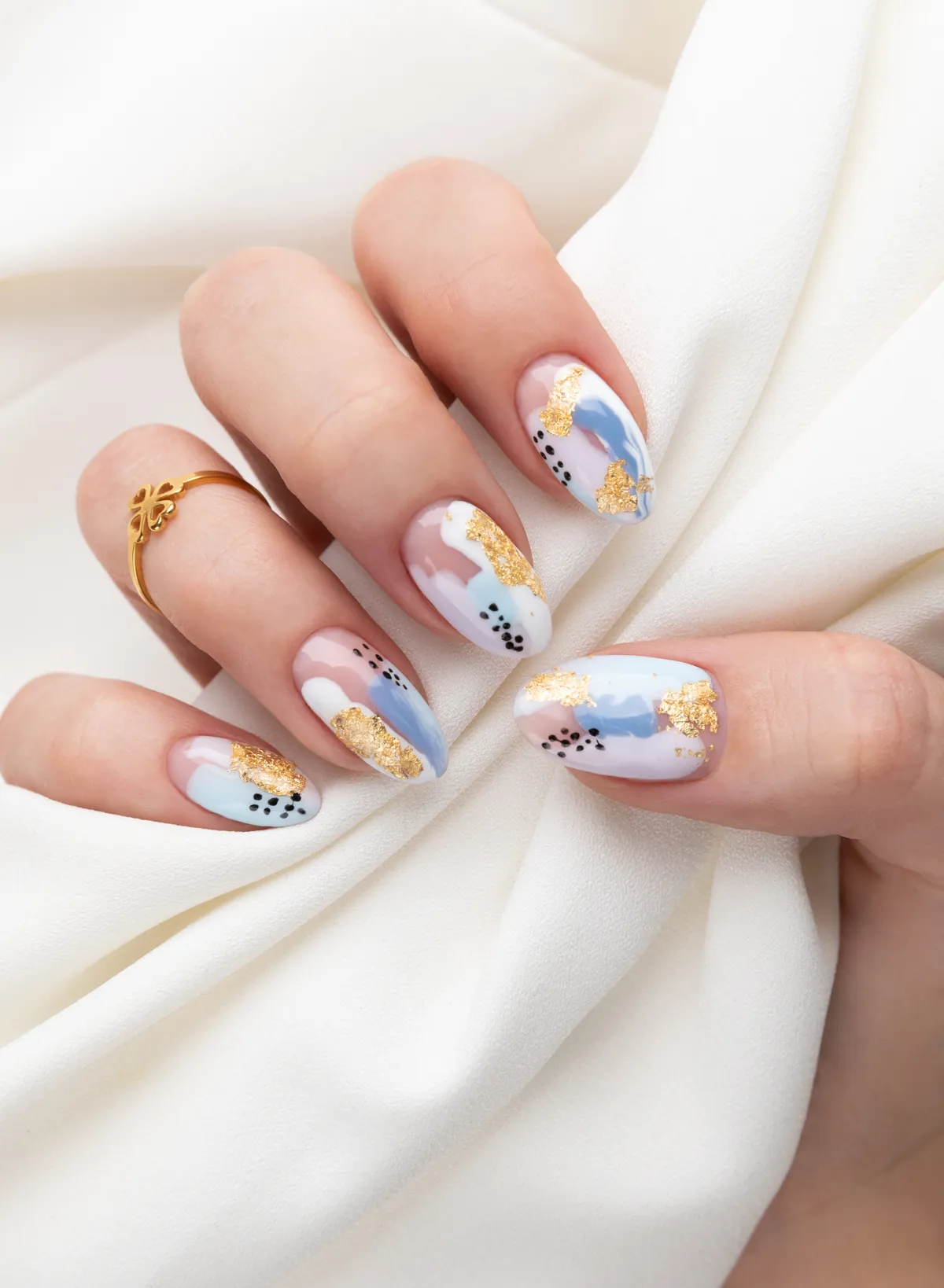 Almond nails with pastel abstract nail art and gold leaf resting on white silk