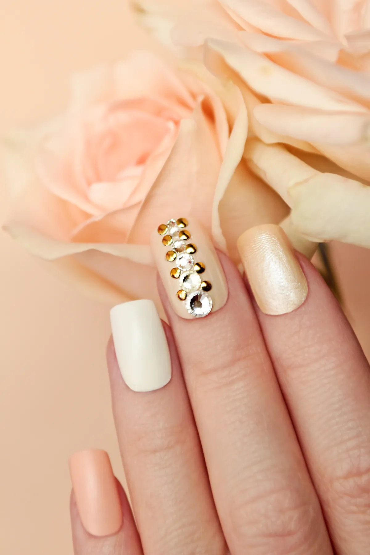 Peach and cream nails with gold studs beside pale roses