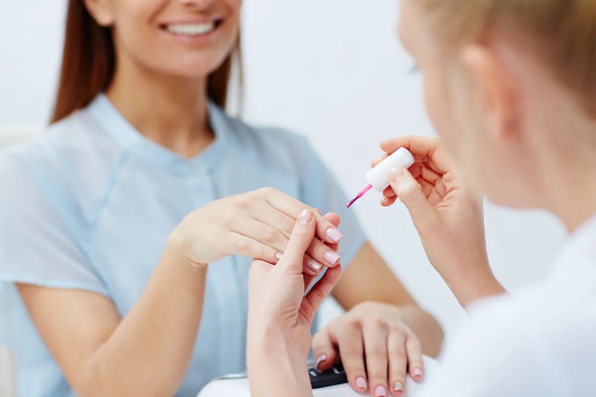 A smiling nail technician painting a client’s nails during an appointment