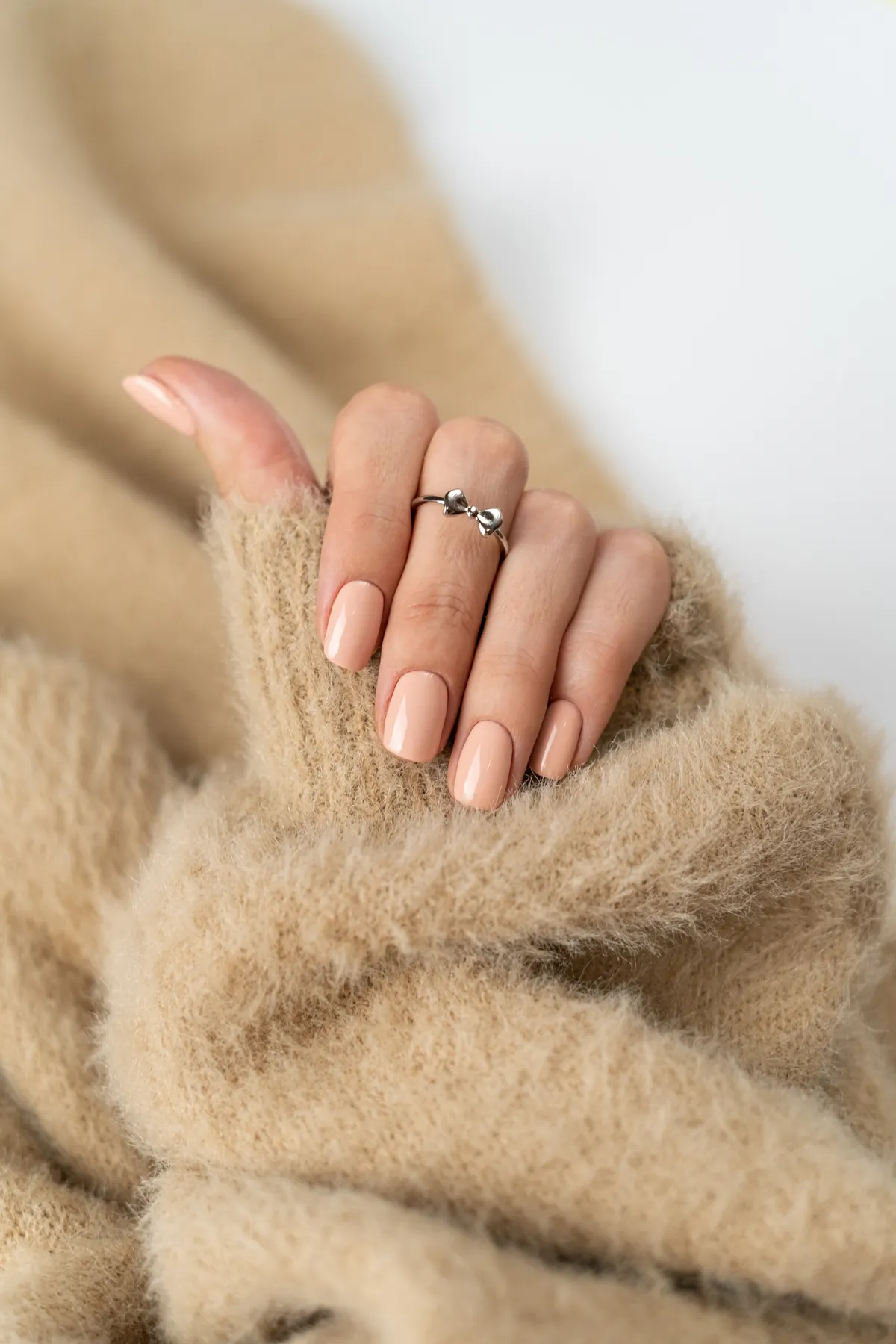 A sheer nude manicure on slim fingers resting on a soft beige knit