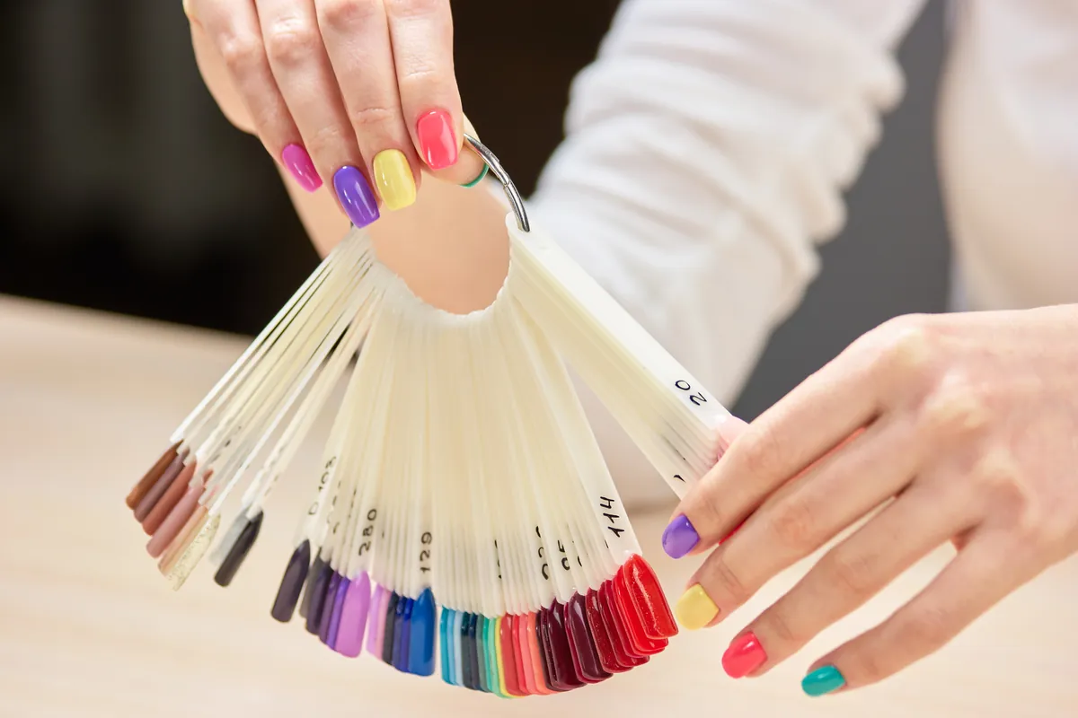 A hand holding a fan of colour samples next to painted nails