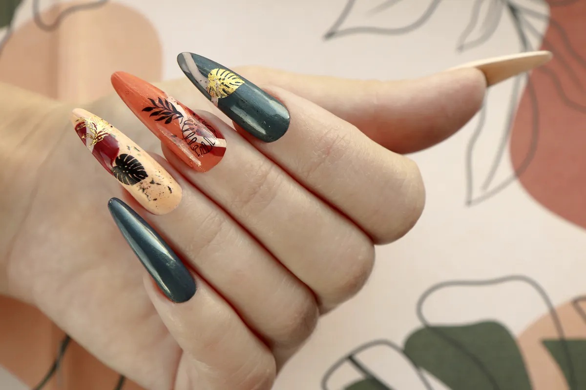 Long almond nails painted in deep green and burnt orange with leaf motifs